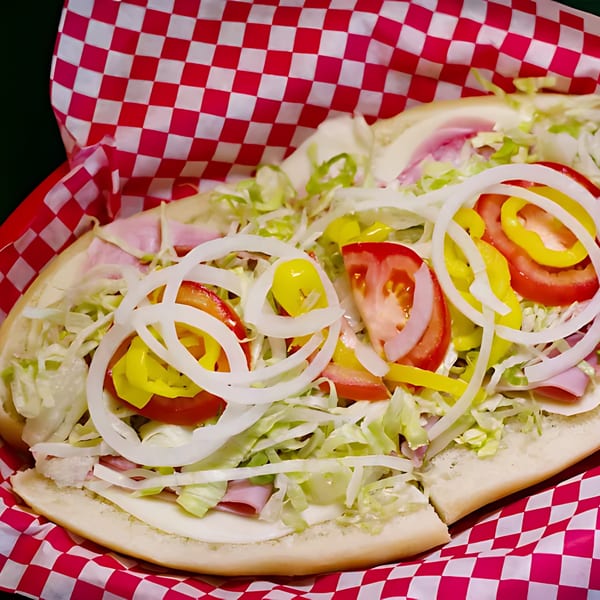 Original Brothers Pizza sub sandwich with ham, cheese, lettuce, tomatoes, onions, and peppers in a red checkered basket.