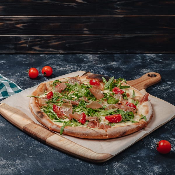 Original Brothers Pizza's pizza with prosciutto, arugula, and cherry tomatoes on a wooden board.