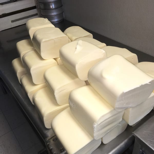 Large blocks of fresh mozzarella cheese stacked on a stainless steel counter at Original Brothers Pizza.