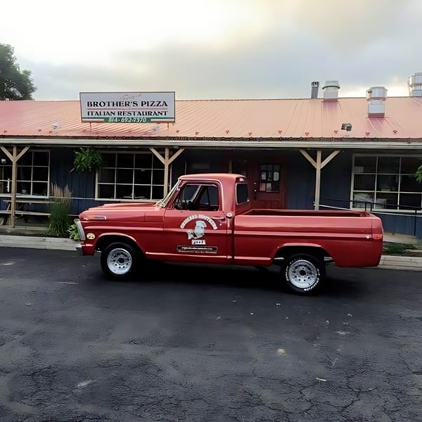 Red vintage pickup truck with Original Brothers Pizza logo parked in front of the restaurant.