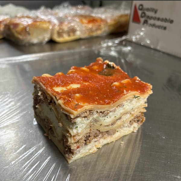 A slice of lasagna with meat, ricotta, and tomato sauce on a metal counter.