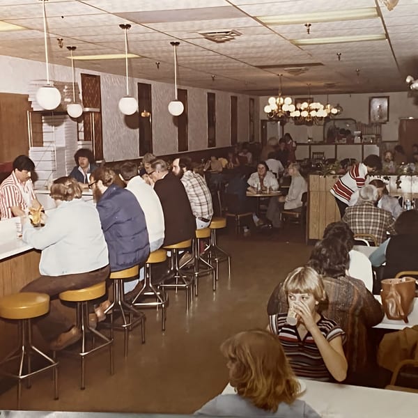 A busy Original Brothers Pizza dining room with customers at the counter and tables in a vintage setting.