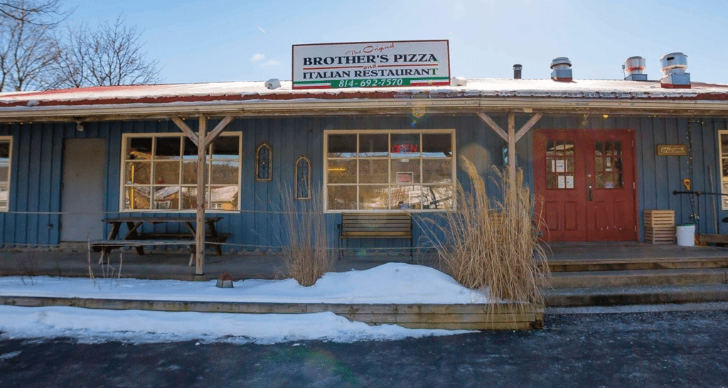 Storefront of Stormstown Brothers Pizza Location. Blue siding, red door, with snow in the forefront.